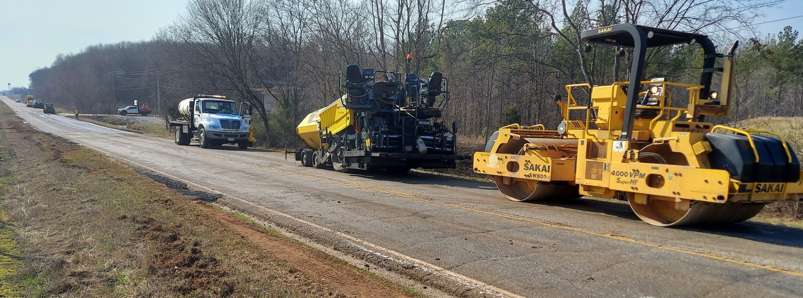 Equipment is lined up to pave a section of road where potholes had been patched.