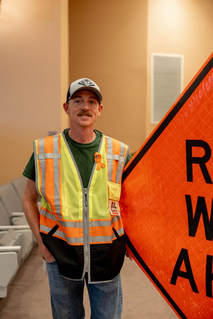 Charlie Posey poses by a Road Work Ahead sign