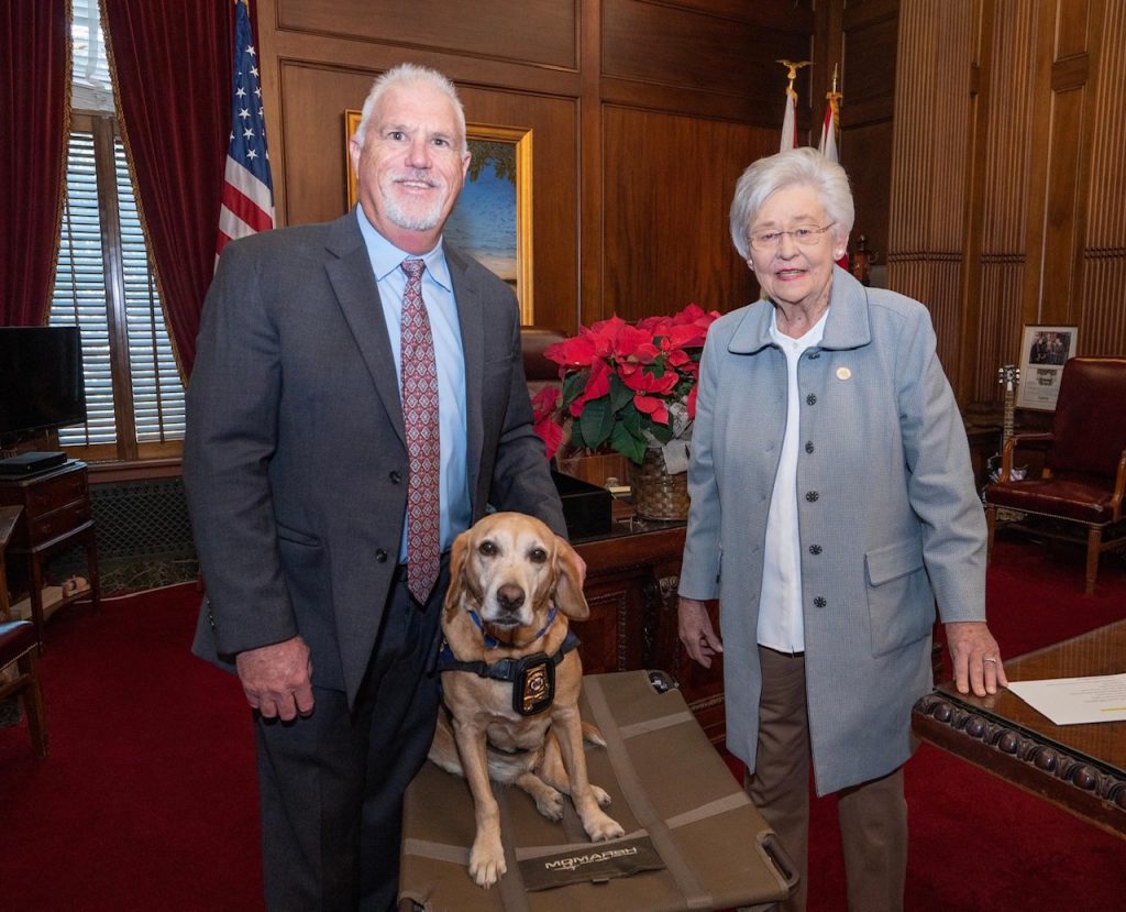 Morris King and Millie, a yellow Labrador Retriever, pose with Alabama Governor Kay Ivey in her office