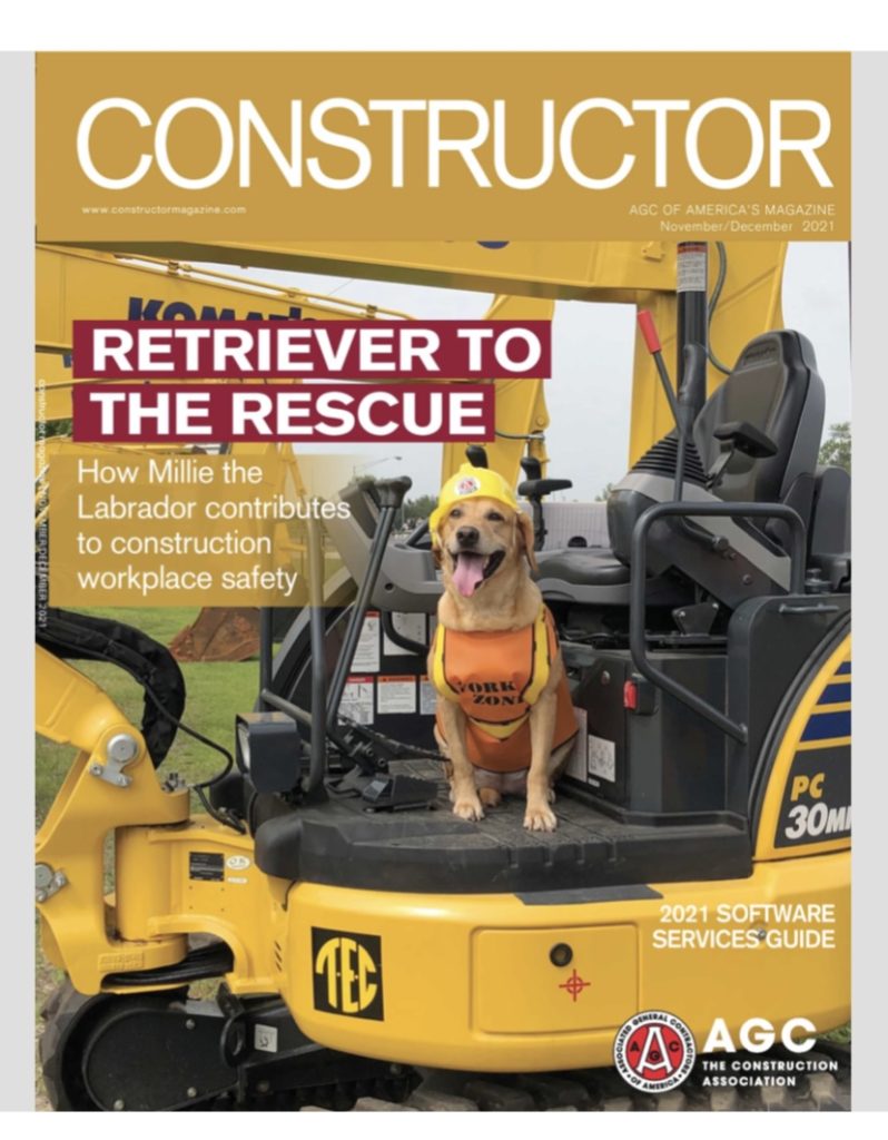 The cover of the November/December 2021 issue of Constructor magazine featuring an image of Millie, a yellow Labrador Retriever, wearing a yellow hard hat and an orange safety vest standing on a tractor with the words Retriever to the Rescue: How Millie the Labrador contributes to construction workplace safety next to her
