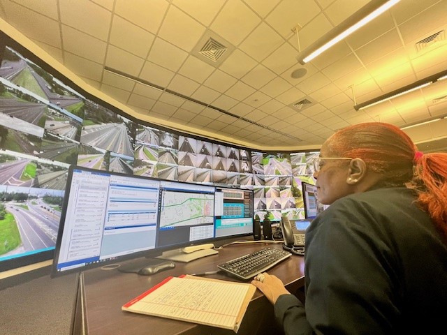 a woman looking at traffic date on monitors with large screens displaying traffic cameras in the background