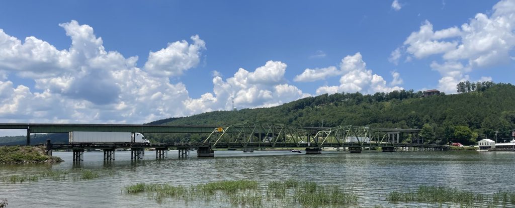 A low, narrow bridge crosses the river with a taller, modern bridge visible in the background.