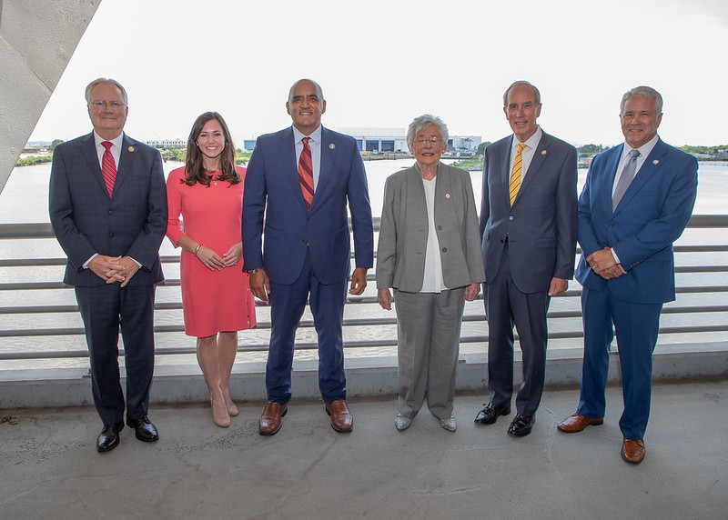 Congressman Jerry Carl, Senator Katie Britt, Federal Highway Administrator Shailen Bhatt, Alabama Governor Kay Ivey, Mobile Mayor Sandy Stimpson, and Fairhope City Councilman Jack Burrell pose in front of the Mobile River