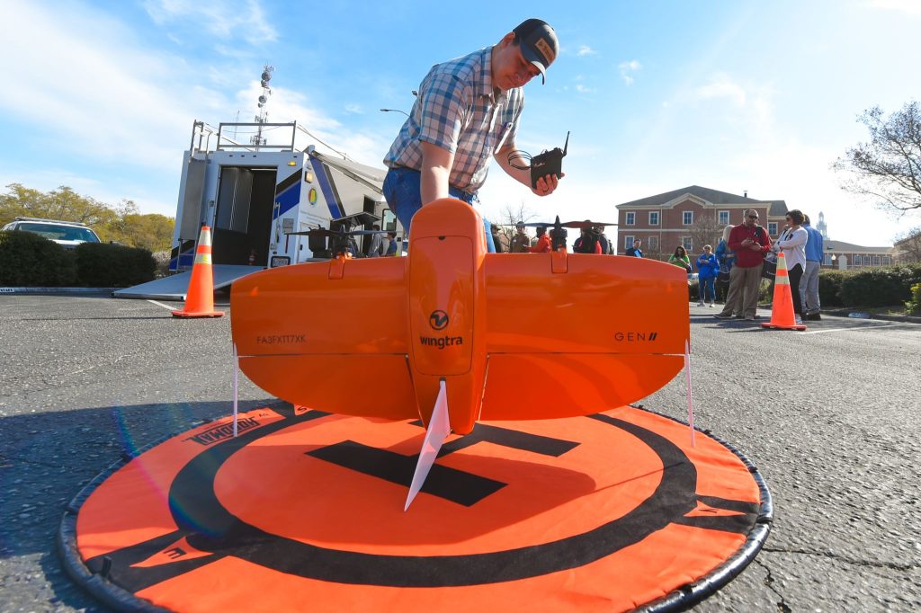 A drone on pavement with guy standing behind it with remote getting ready to fly it.