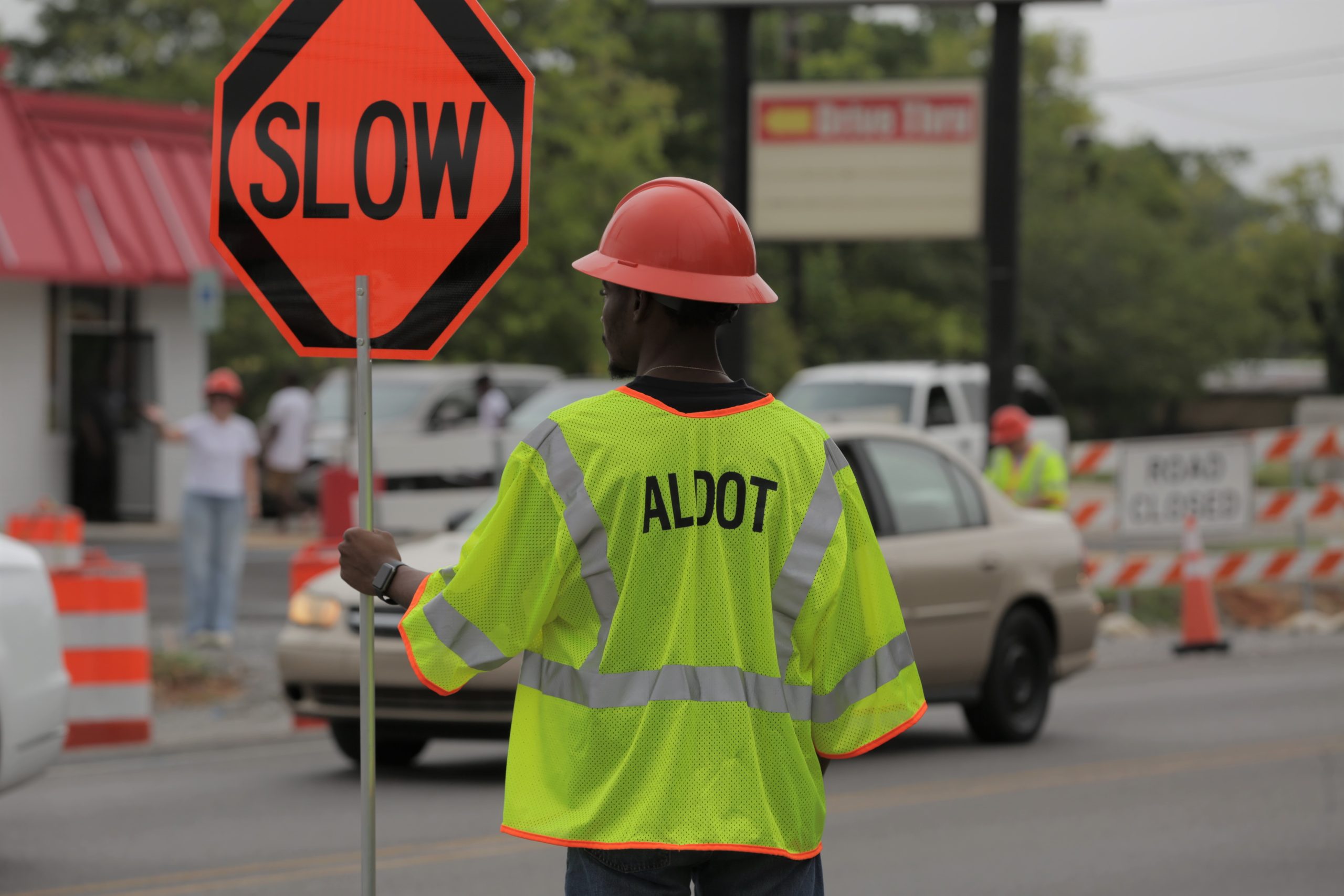 Road worker in safety vest holding sign with the word "slow" inside of a work zone.