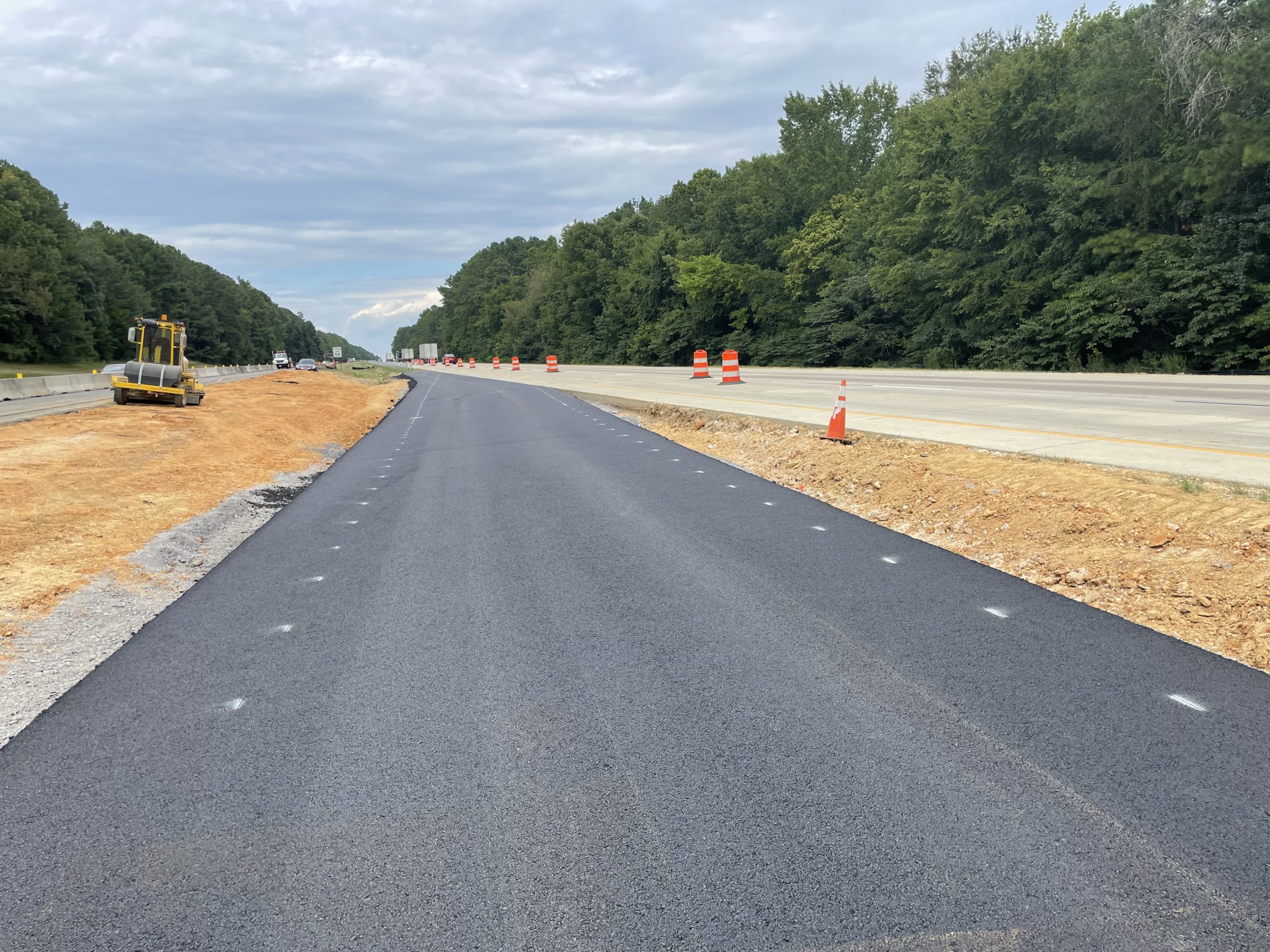 A fresh asphalt lane extends through the median between roadways,