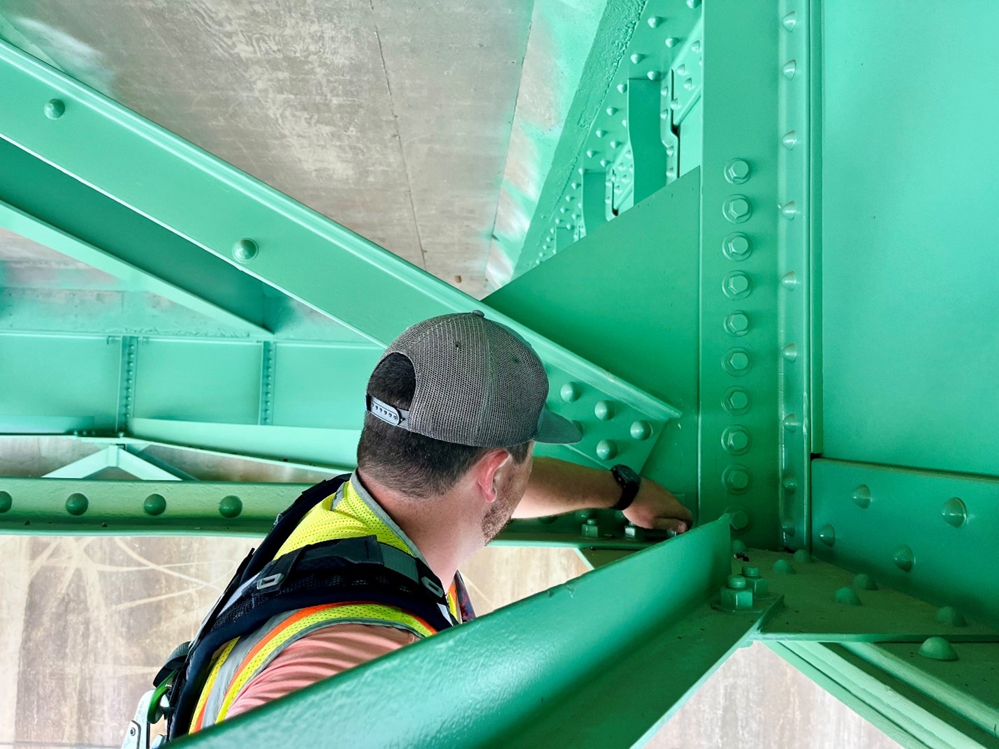 Man inspecting bolts under a bridge