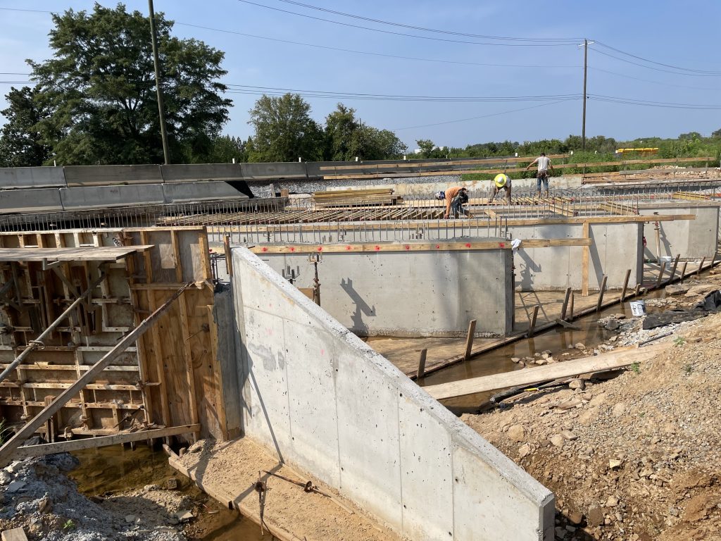 Workers position boards and plywood on top of a large concrete structure.