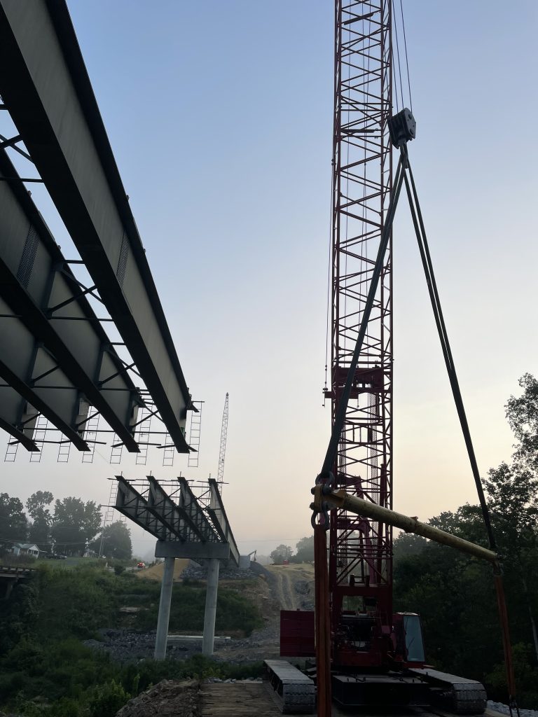 A crane stands beside the bridge. The center section of girders is not yet in place.