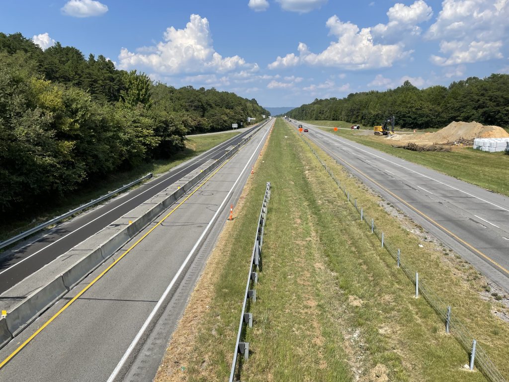 Two roadways viewed from above. On the left is the northbound roadway with concrete barrier running down the middle.