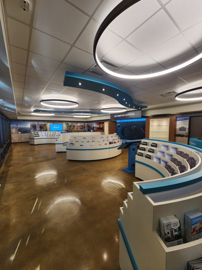 A room with polished concrete floors, circular light fixtures, and curved racks filled with brochures.