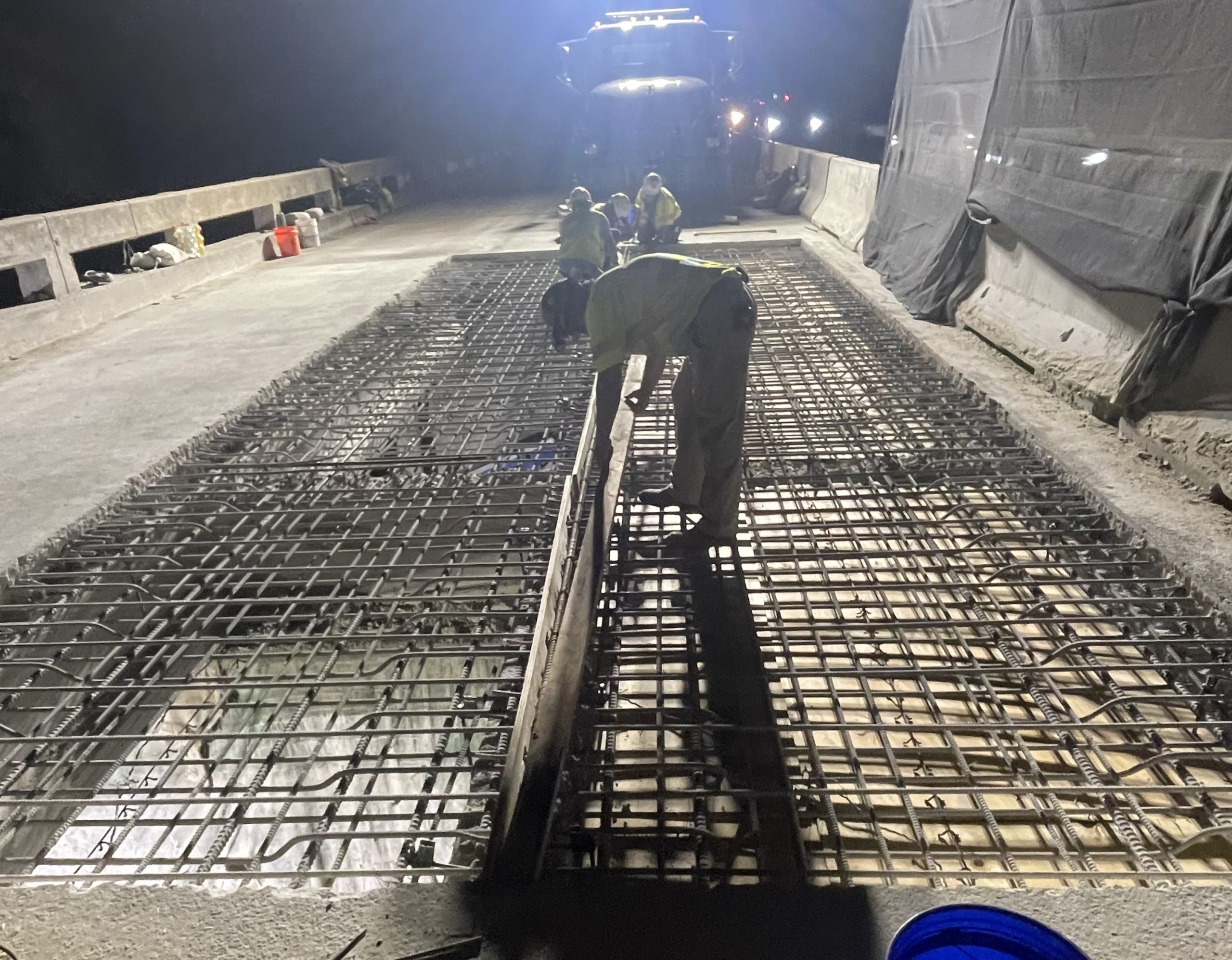 People working at night on a bridge deck with a large rectangular section of exposed rebar.