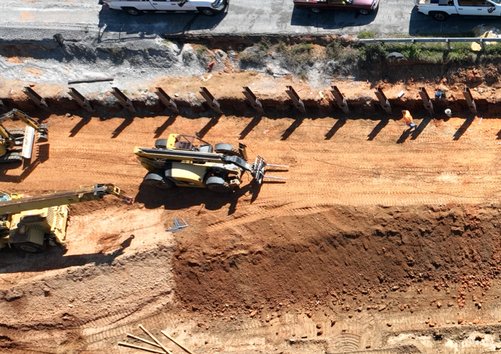 Aerial view of the construction of a soldier pile retaining wall to stabilize the shoulder and prevent further landslide activity in the area.