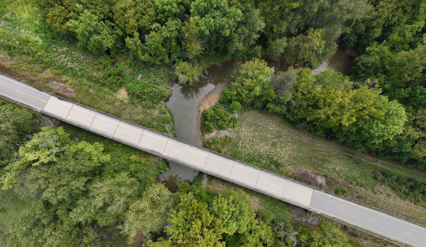 A view of bridge from above. A creek passes underneath the bridge.