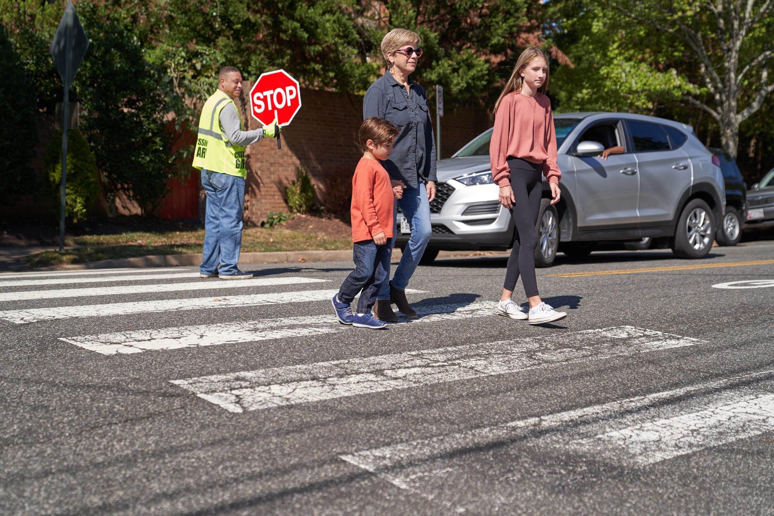 National Pedestrian Safety Month image with a crossing guard stopping traffic so a family can cross in a cross walk.