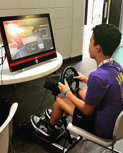 Student at a driving simulator. Steering wheel connected to pedals in a class room. Student looking at screen.