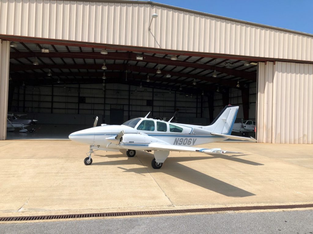 Picture of a small airplane parked in front of an airport hangar.