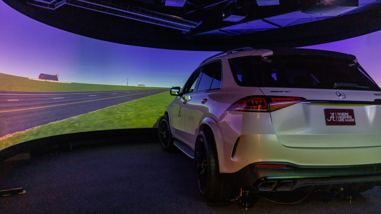 White SUV in front of large screen displaying simulated rural road.