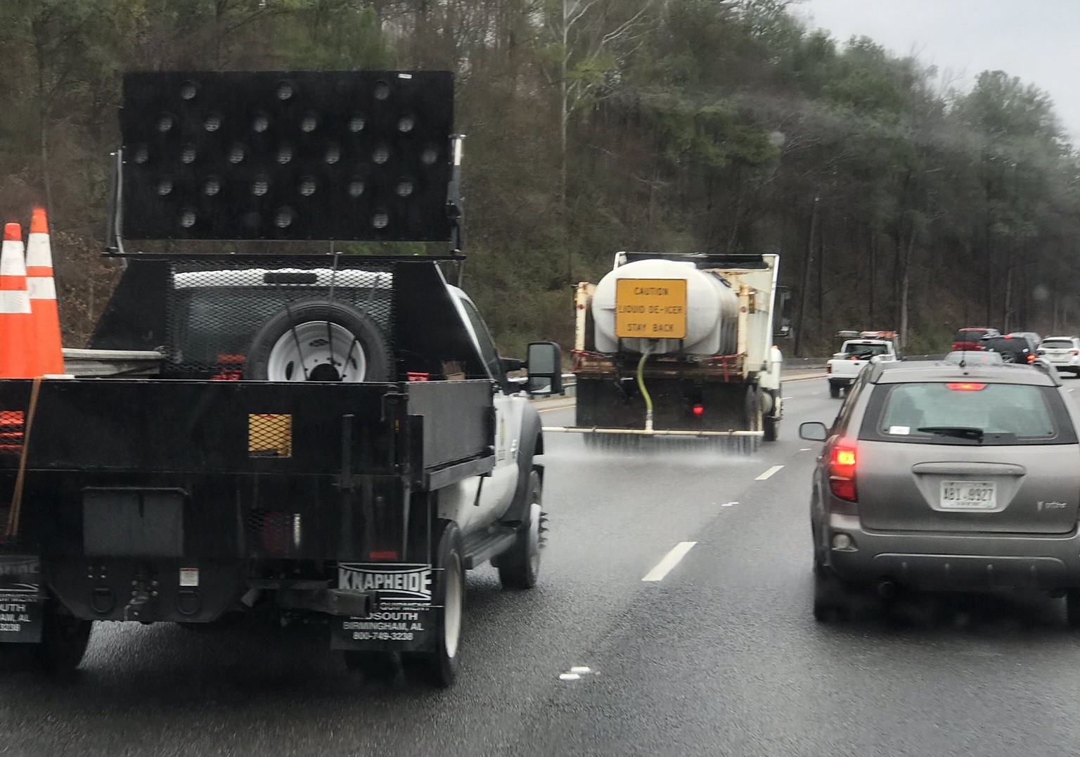 Two service trucks salting a roadway with vehicles in the lane beside them