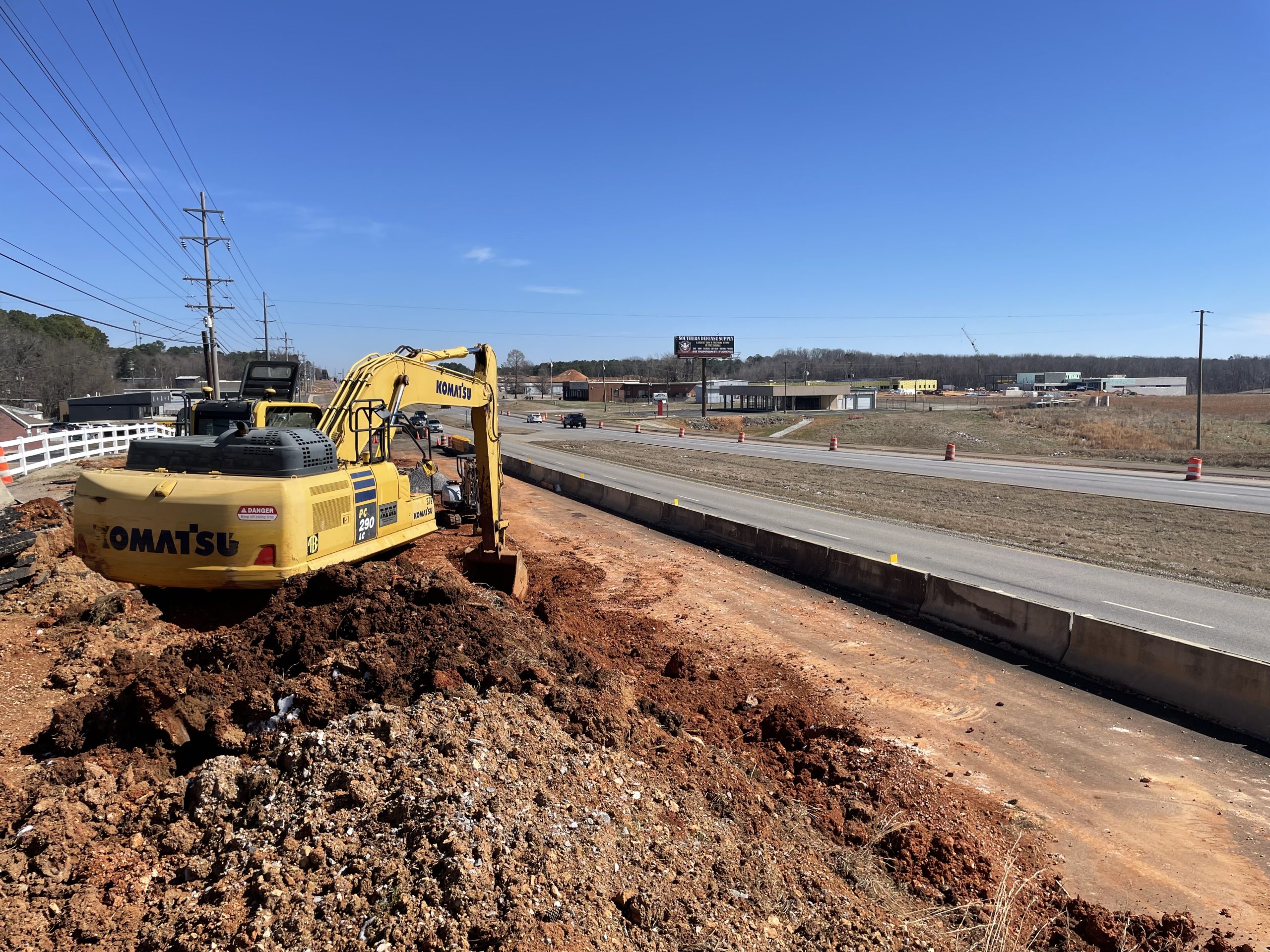 An excavator works behind a concrete barrier next to a roadway.