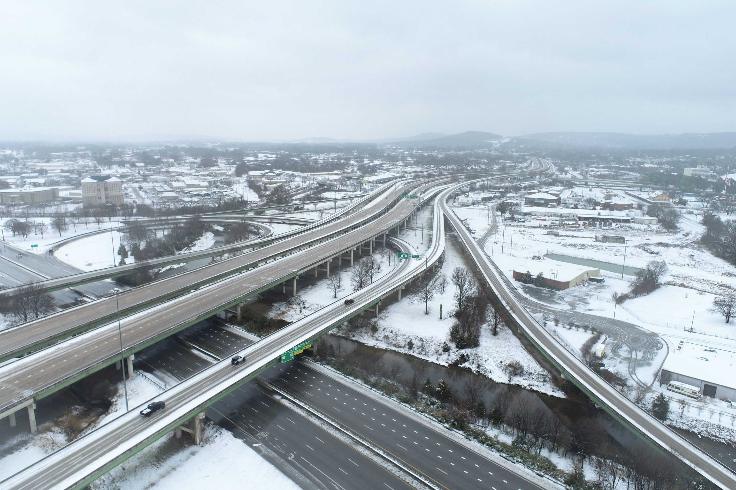 An aerial view of an elevated roadway interchange. Surroundings are covered in snow.