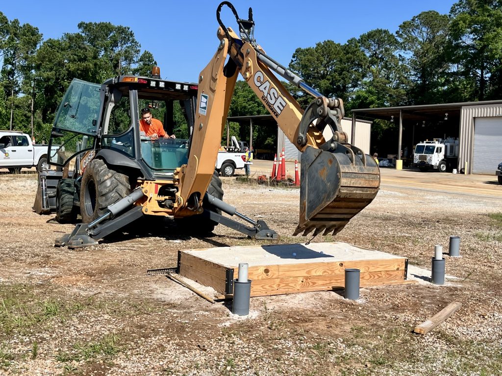 A backhoe with a spoon-like attachment picking up a golf ball out of the sand.