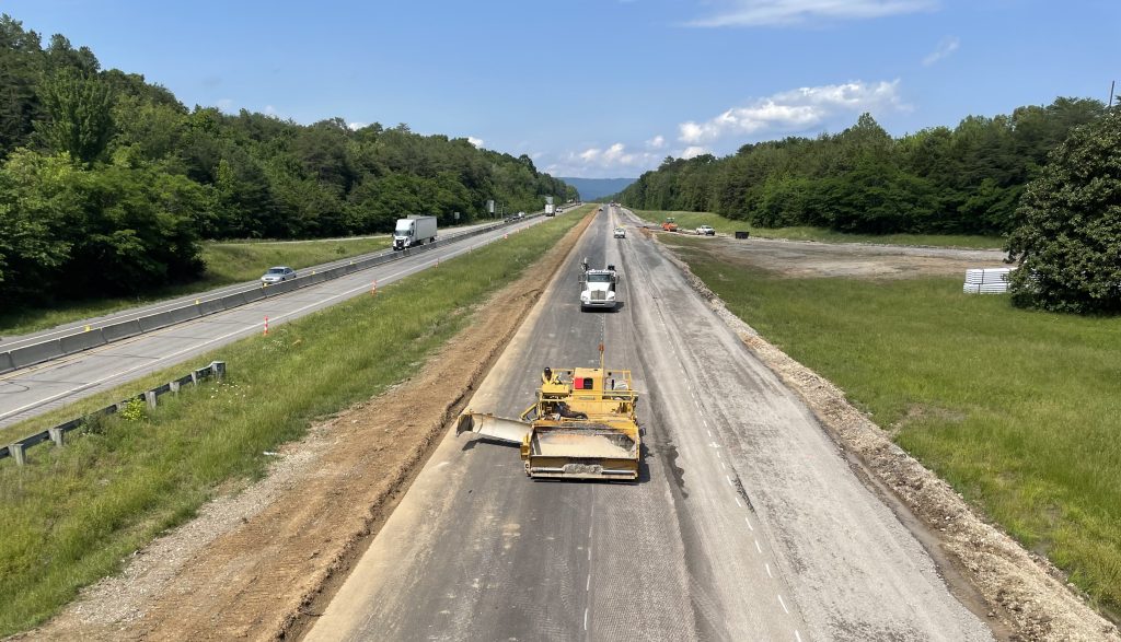 Construction equipment travels on a closed roadway that has recently been paved.