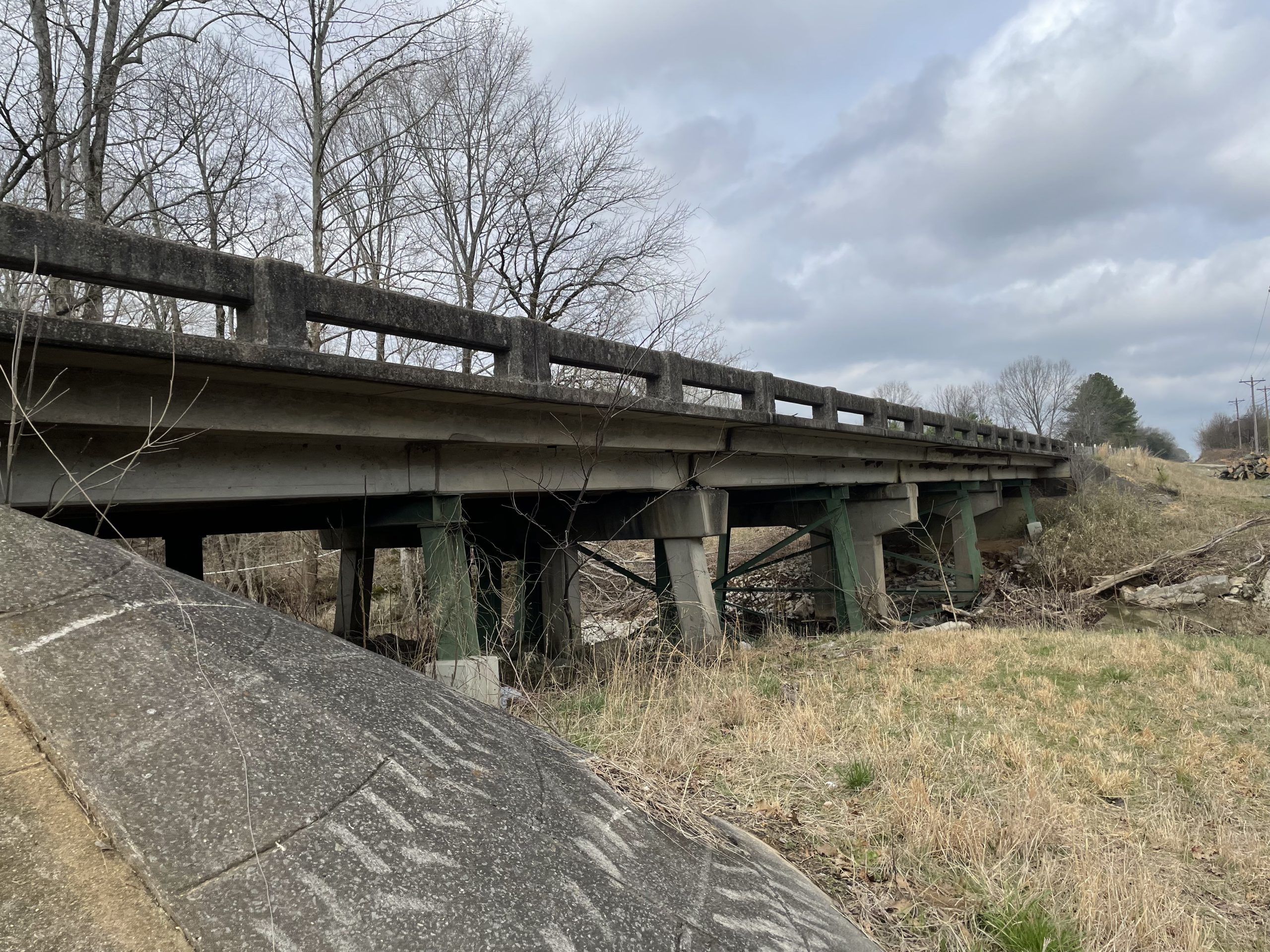 The side of a weathered bridge, viewed from a creek bank.