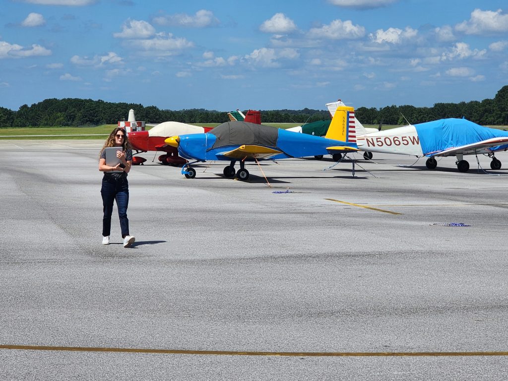 Airport inspector walking inspecting the taxiway pavement with airplanes in the background.