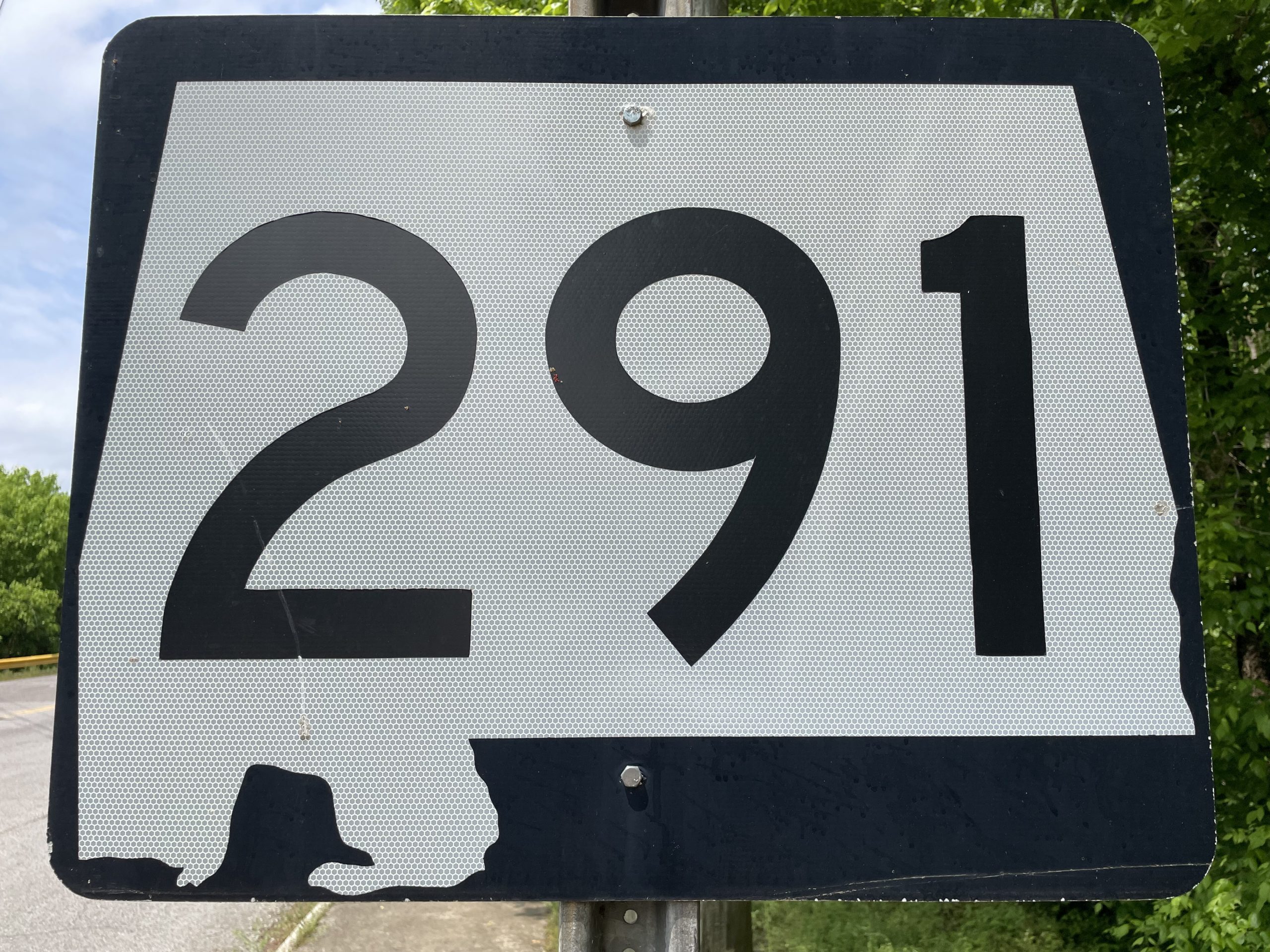 A highway sign with black number 291 inside white outline of the state of Alabama on a black background.