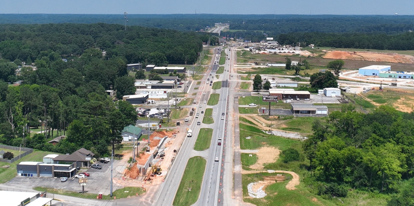 An aerial view of a divided four-lane road. Construction of additional lanes and retaining walls are visible.
