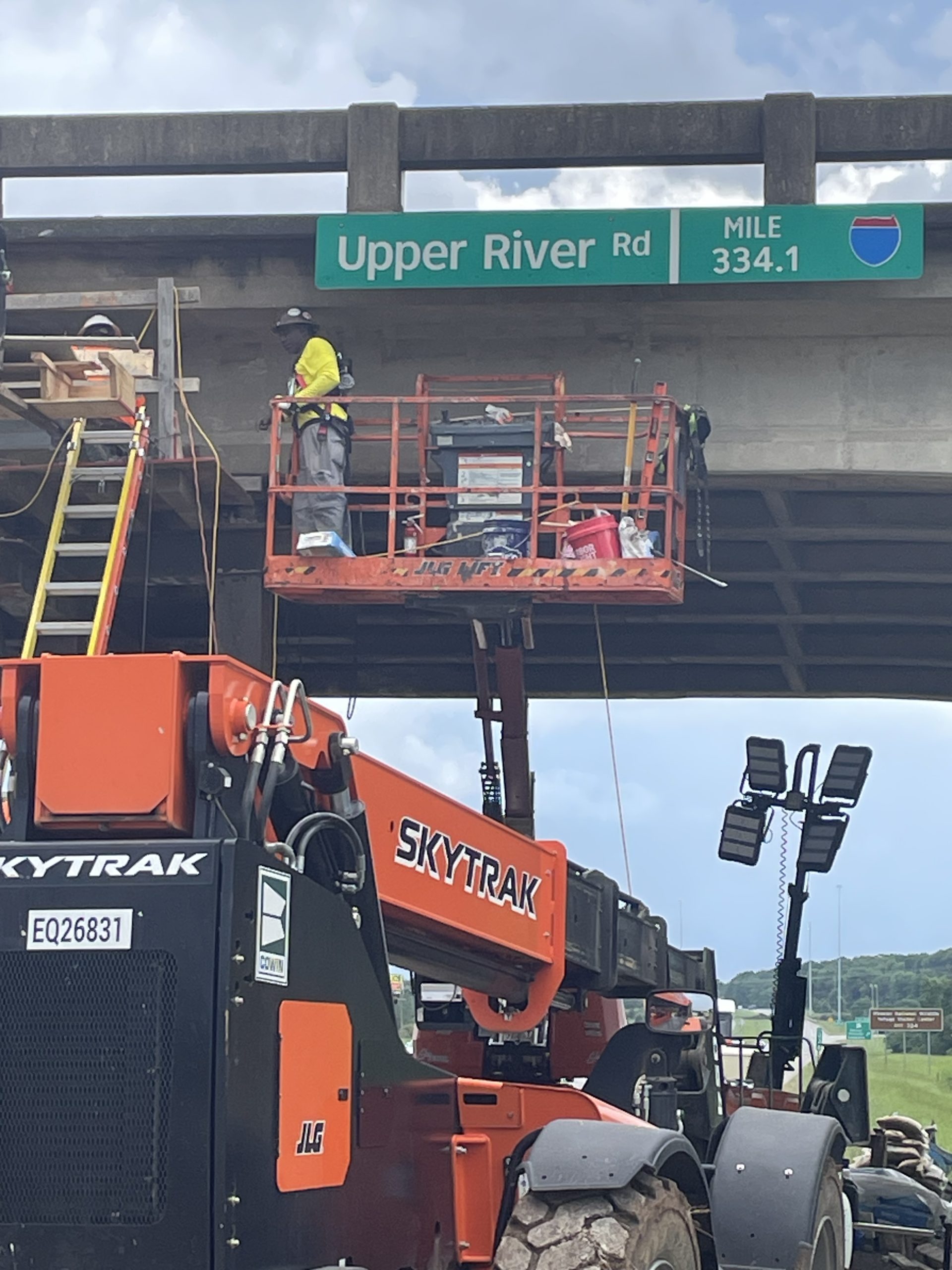 Workers on a lift and scaffolding working repair a bridge.