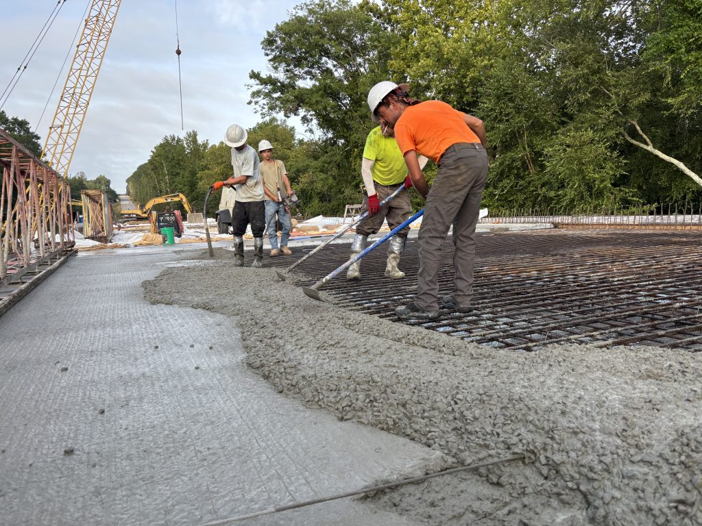 Workers use tools to spread freshly-poured concrete.