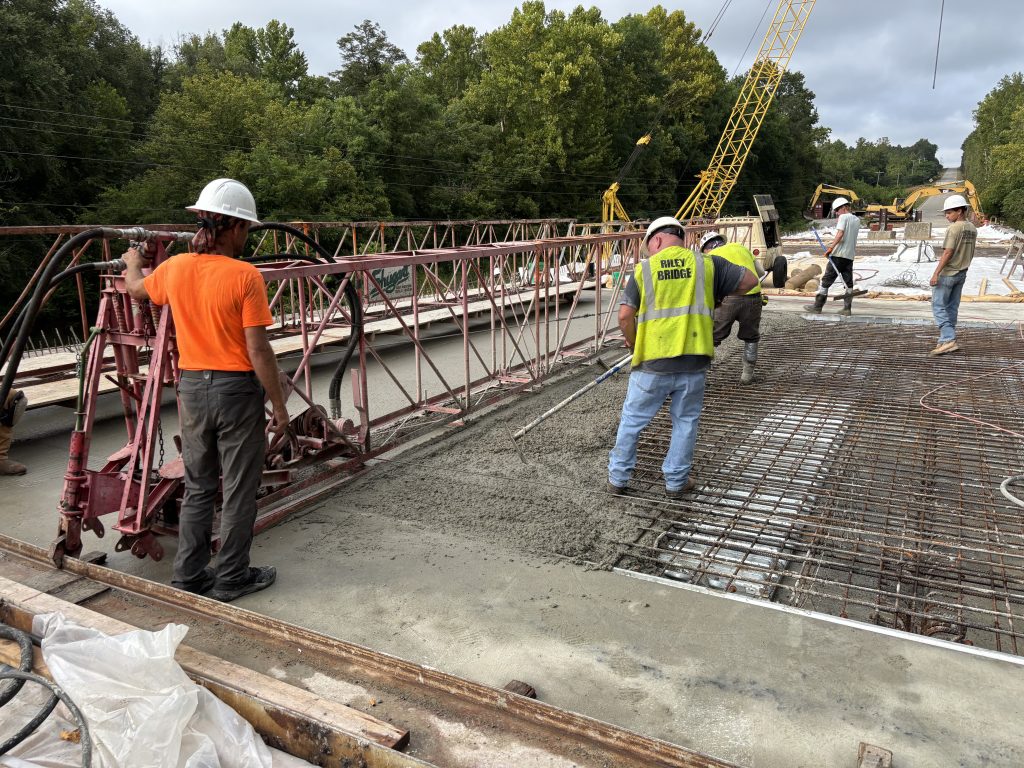 A man operates a large metal device positioned on top of the of the wet concrete.