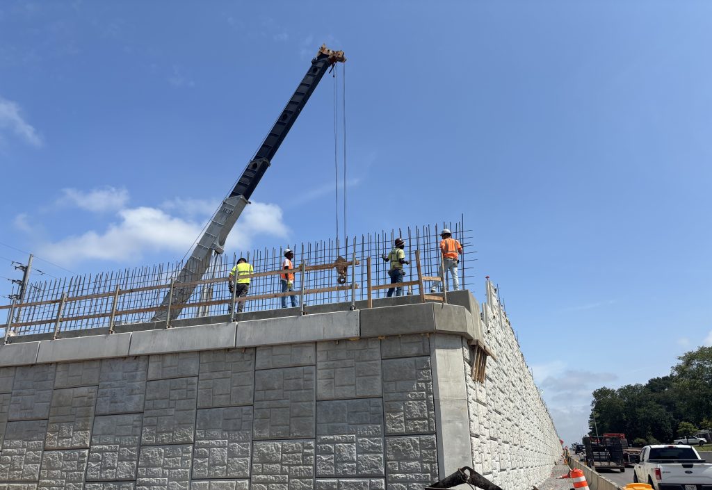 Workers work with rebar atop a bridge abutment and mechanically stabilized earth retaining wall.
