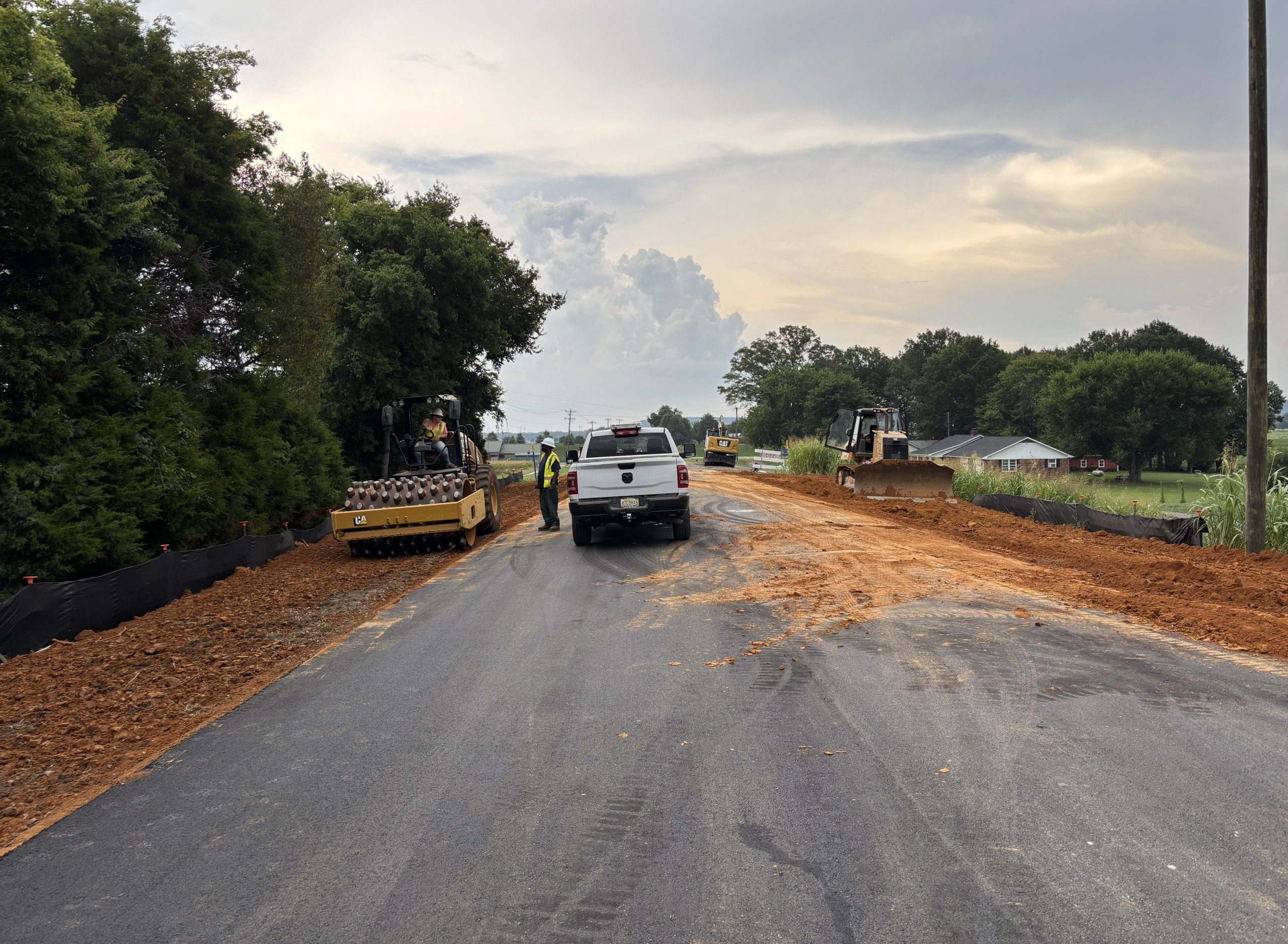 Workers and equipment on the shoulders of a freshly-paved road.