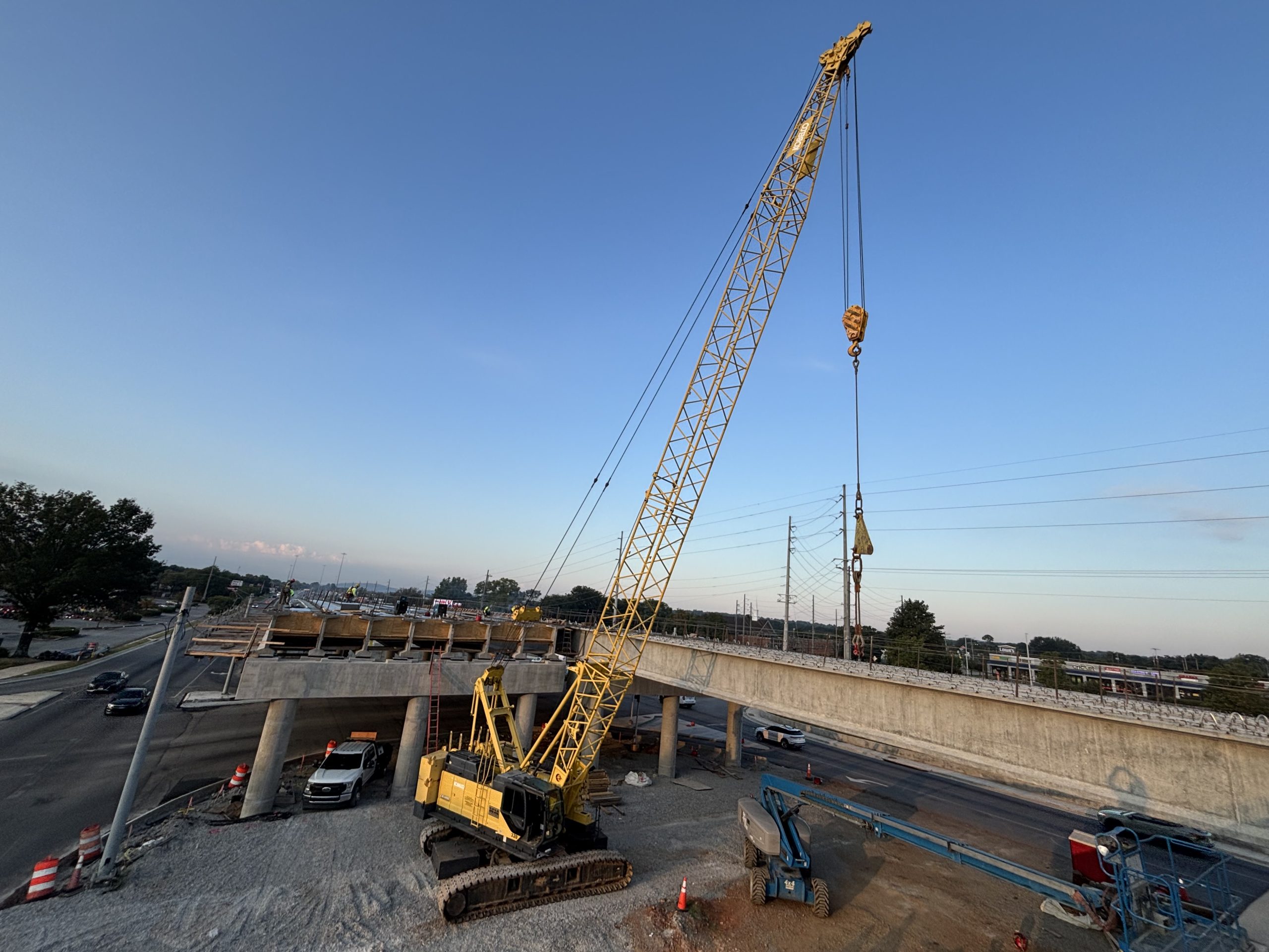 A crane sits beside an incomplete bridge, the girders of which span a roadway.