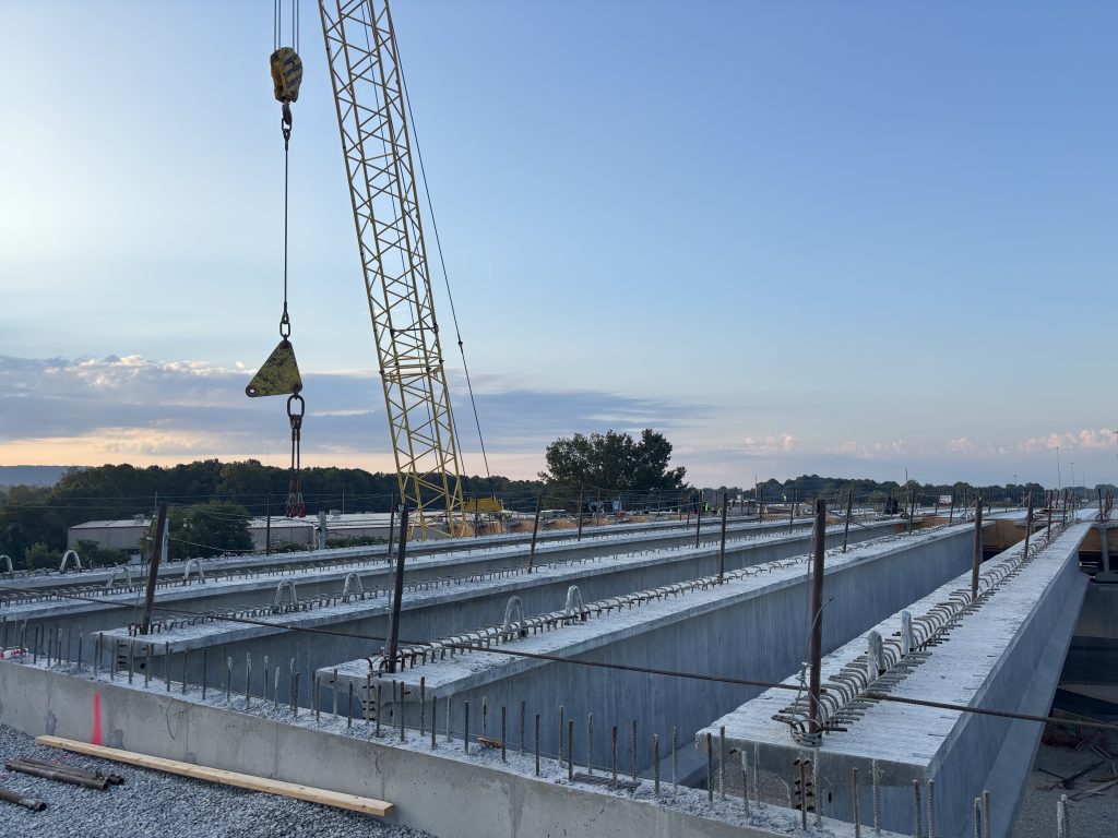 A row of bridge girders, with a crane extending into the sky in the background.