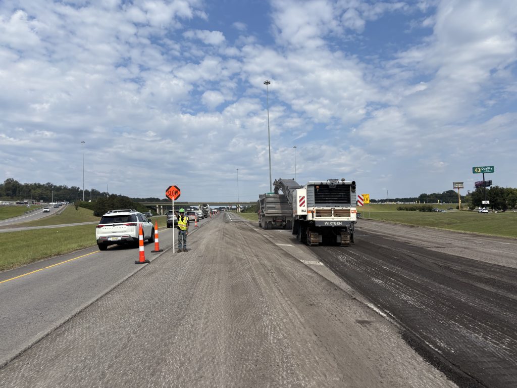 A flagger stands beside the work area with a sign reading: SLOW