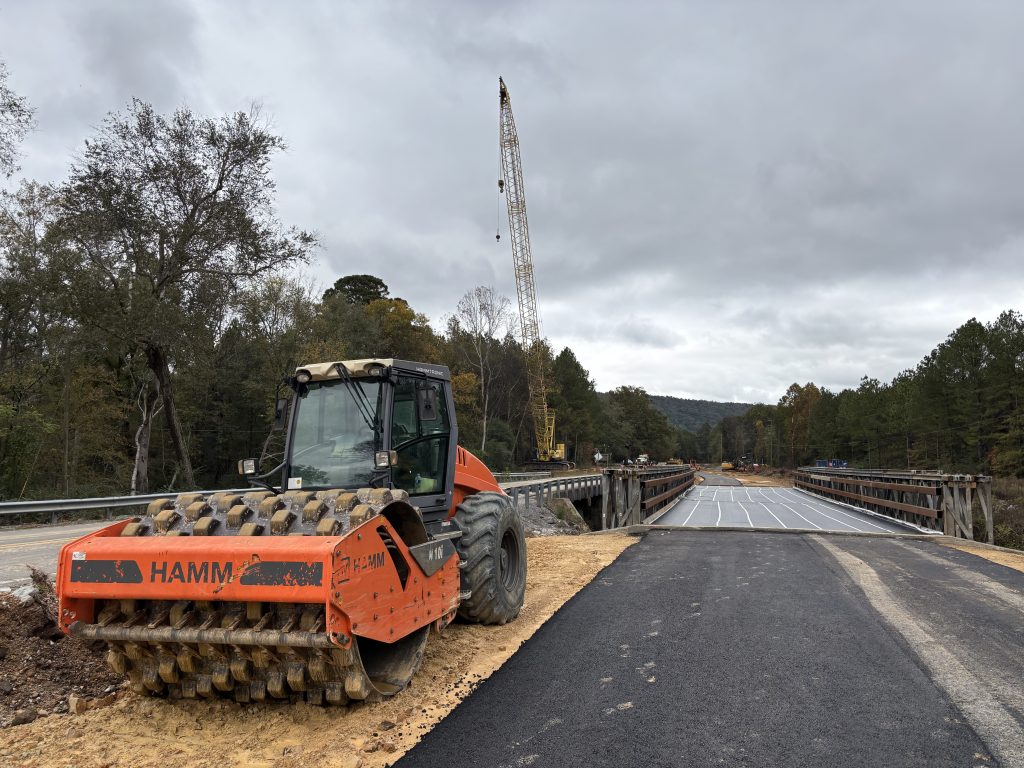 A roller used for soil compaction sits next to a modular bridge. A crane is in the background.