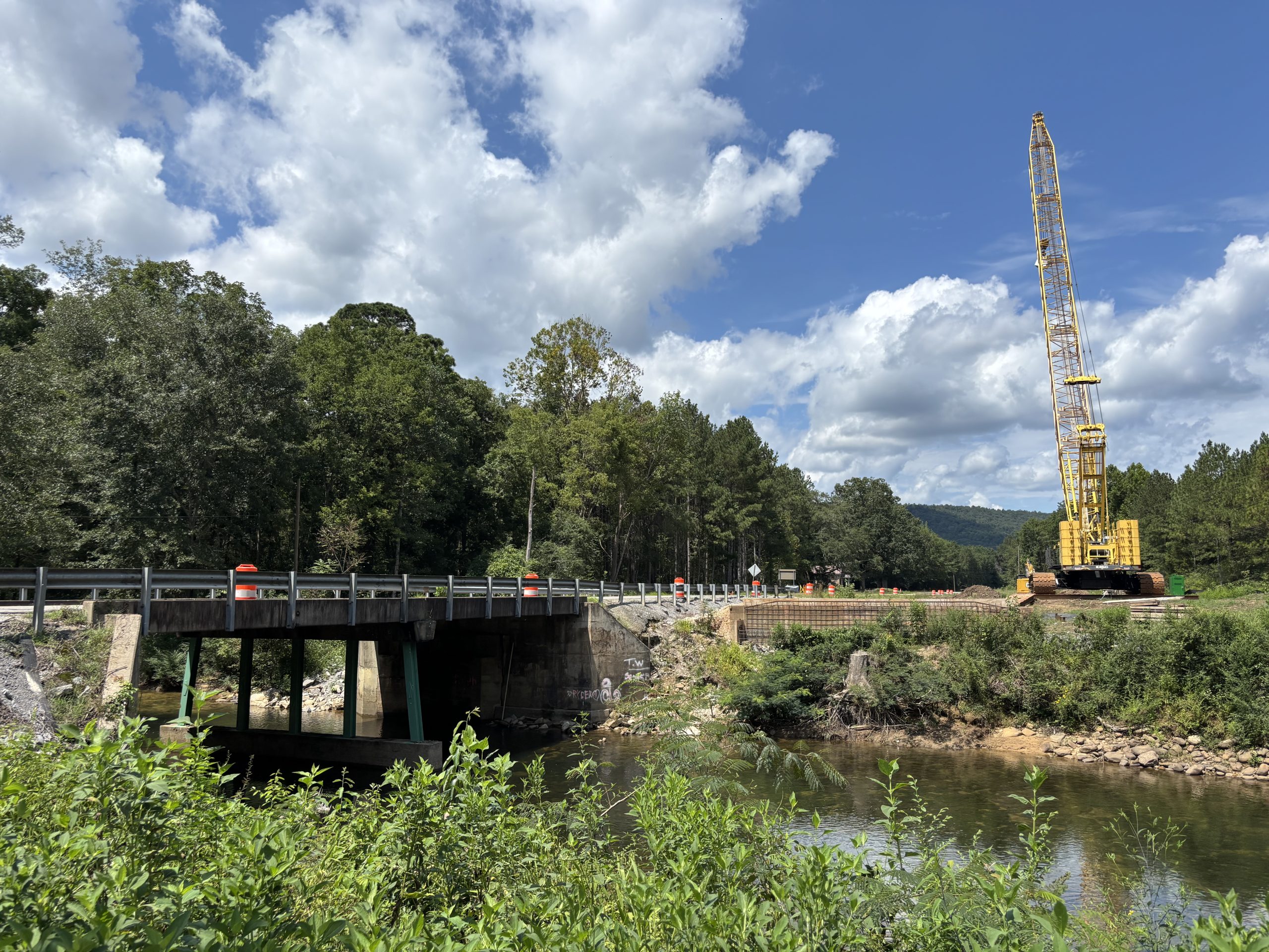An old bridge over a creek. A crane sits on the far bank.