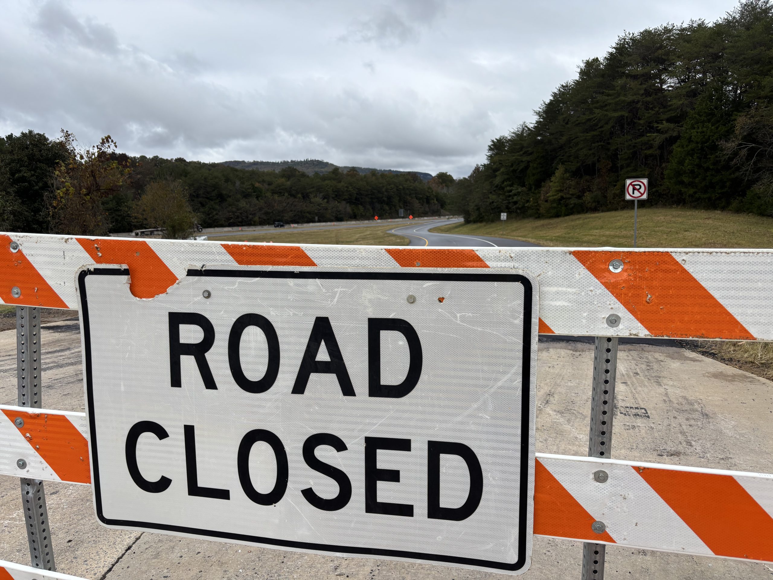 A sign reading ROAD CLOSED on an orange- and white-striped barricade at the entrance to a highway on-ramp.