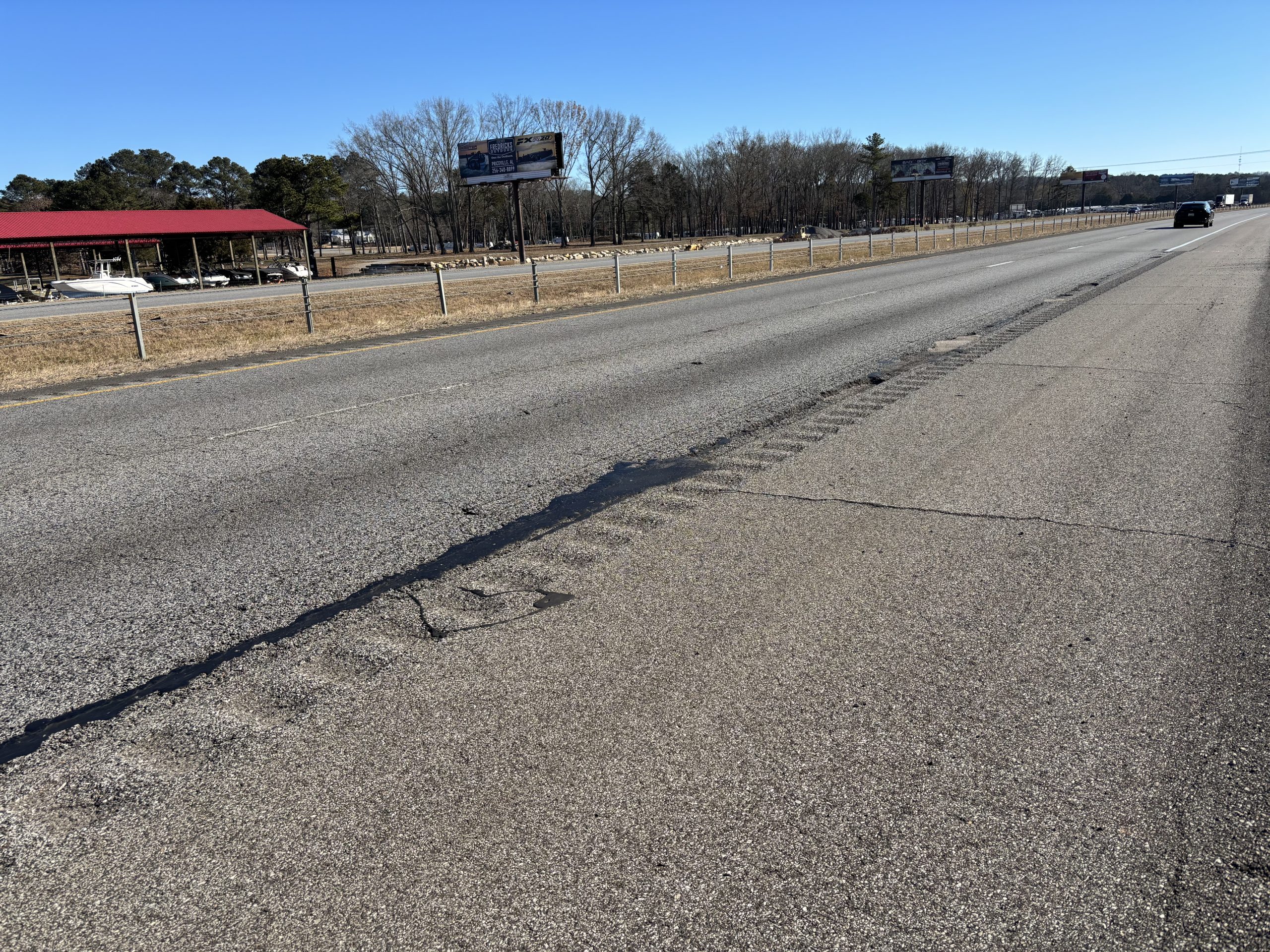 A road with potholes along the outer edge of the travel lane.