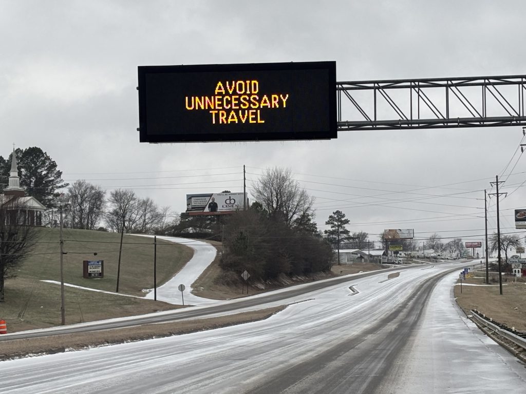 An overhead message sign reads "Avoid Unnecessary Travel"