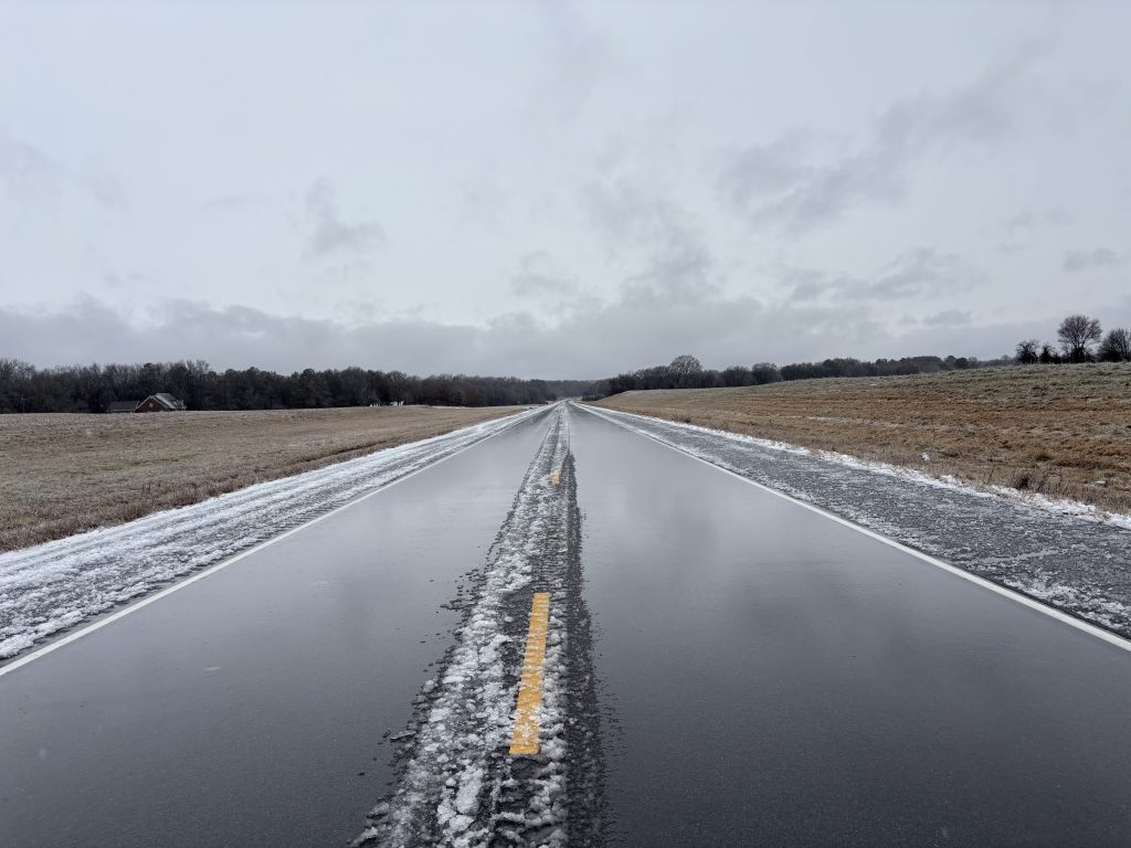 A wet but clear roadway with windrows of ice down the centerline and shoulders.