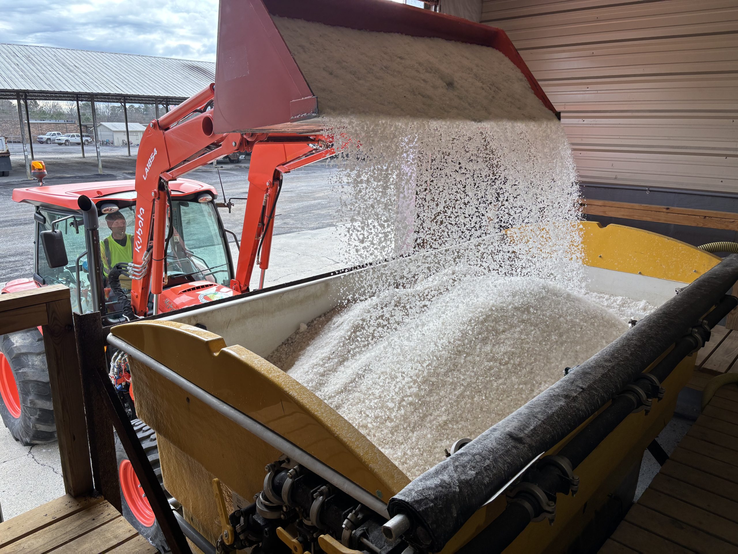 A front loader dumps salt into a brine-mixing tank