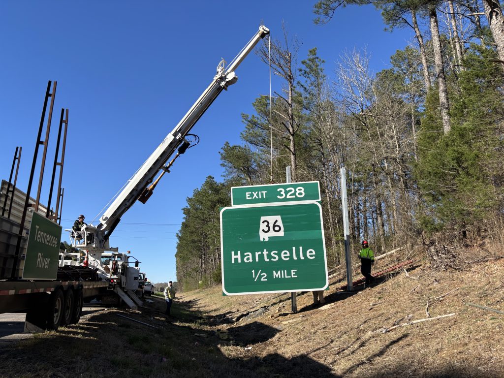 A crane truck lifts a green sign assembly for the half mile notification for Exit 328 SR-36 in Hartselle.