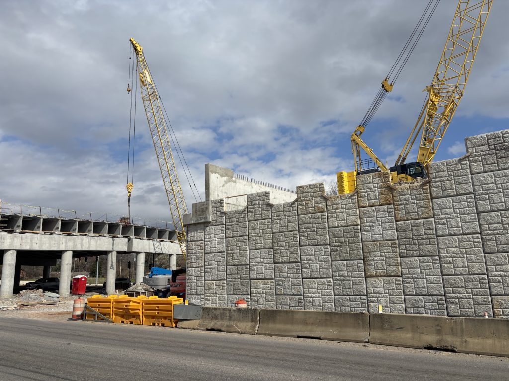 The overpass and mechanically stabilized earth walls that form the slope behind to the south bridge abutment, viewed from the service road.