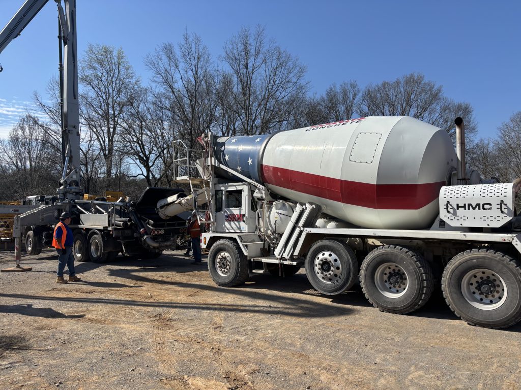 A mixer truck arrives onsite and transfers concrete to the boom pump truck.