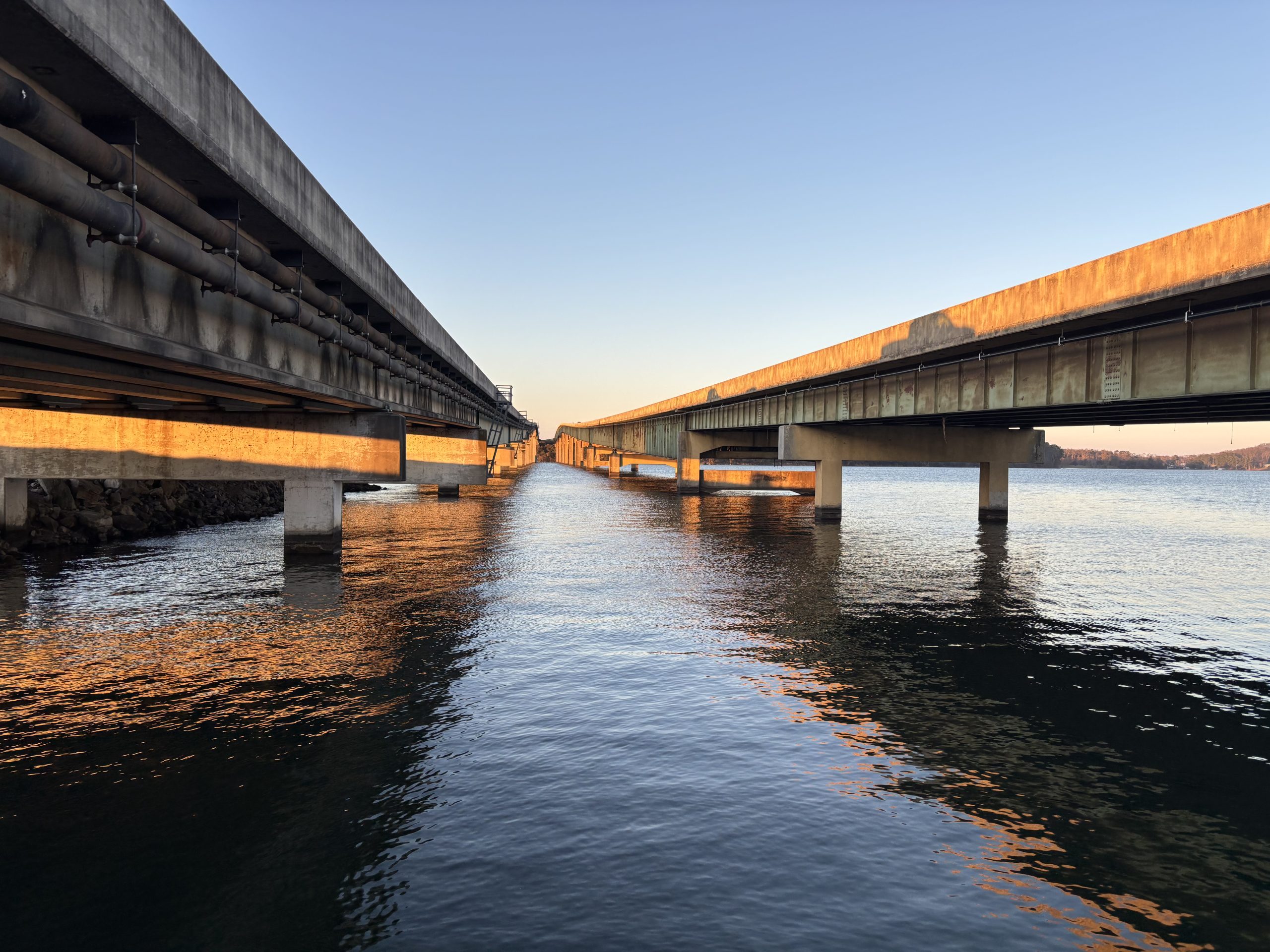 The US-431 bridges in Guntersville are viewed from between the bridges on the south bank of the Tennessee River. The shadows of vehicles traversing the southbound bridge are cast on the side of the northbound bridge by the late afternoon sun.